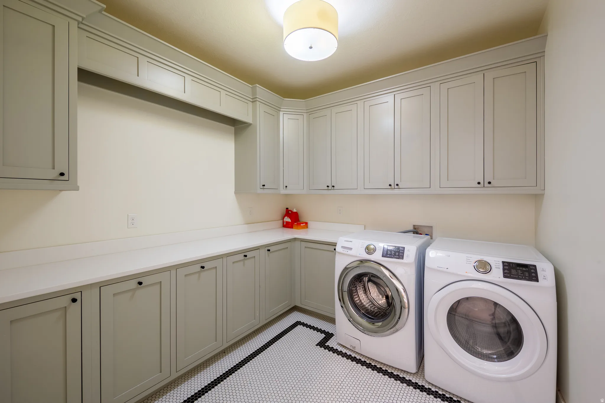 Dedicated utility room featuring extensive built-in cabinetry, wide countertops, hexagonal tile flooring with a black border, a built-in recessed area for appliances, and a flush mount light fixture