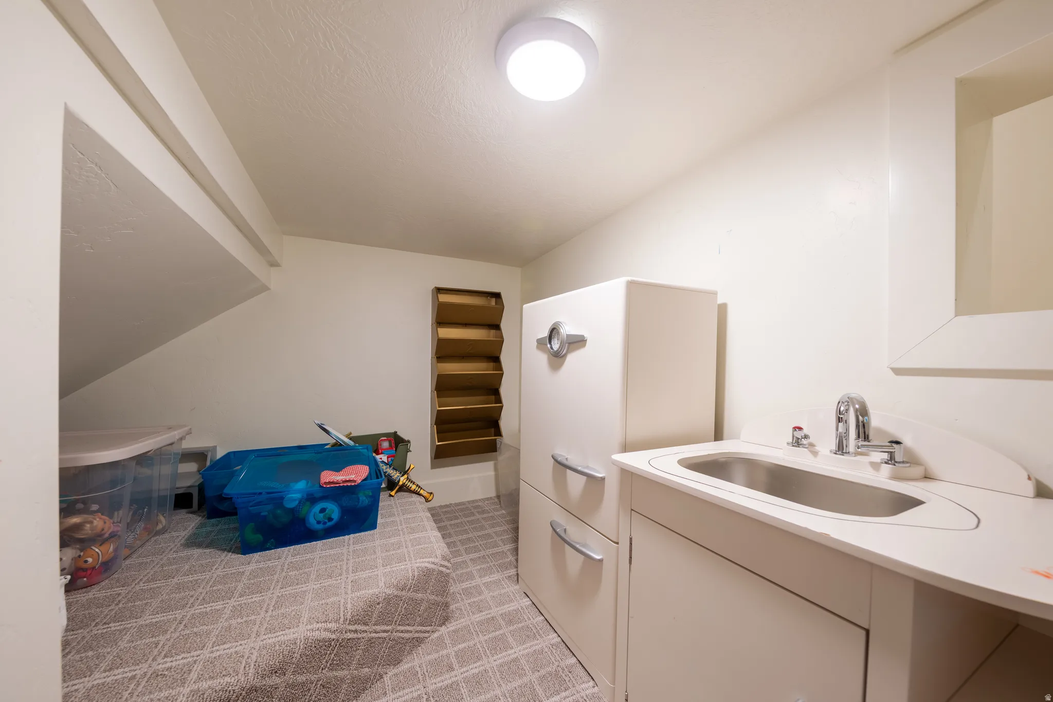 Compact utility space featuring a built-in sink with a chrome faucet, overhead flush-mount lighting, and patterned floor tile