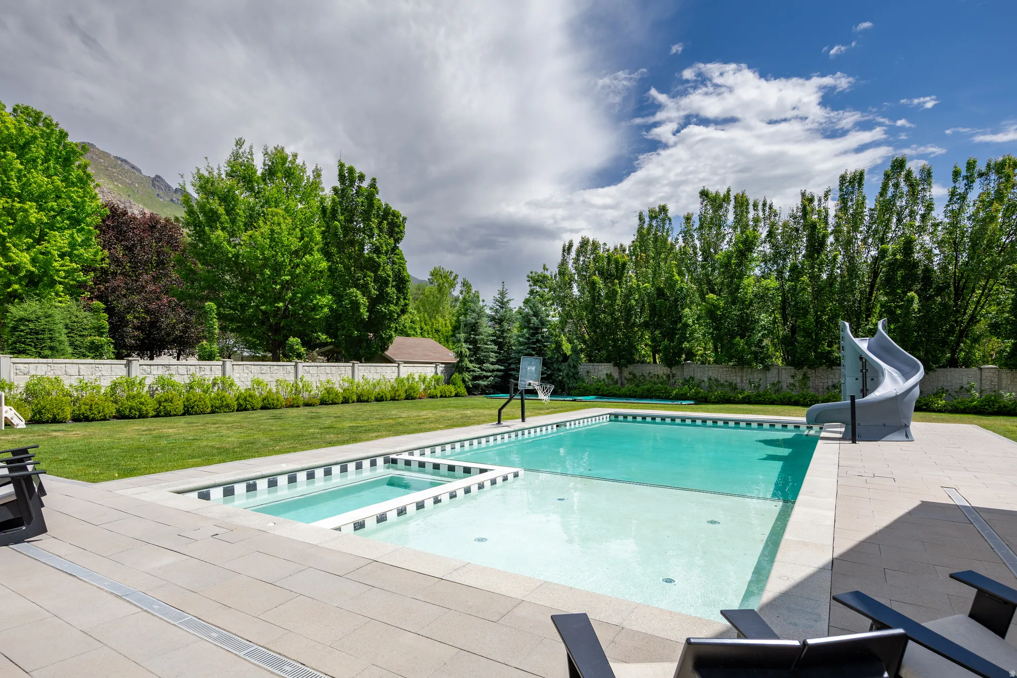 Expansive backyard featuring a rectangular swimming pool with an integrated spa, a built-in pool slide, and a basketball hoop