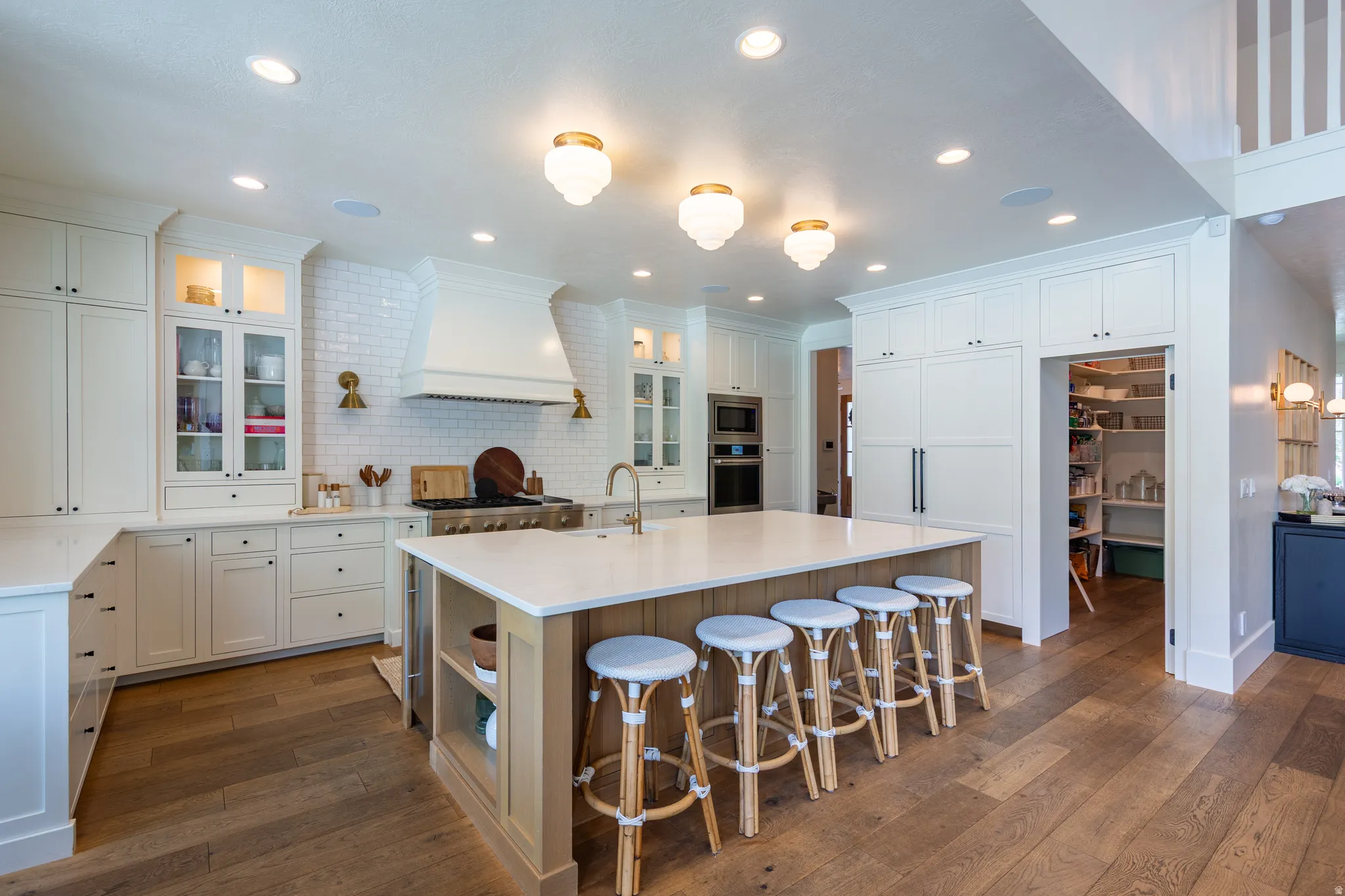 Gourmet kitchen featuring a large central island with a light-toned wood-finish base, ample white cabinetry, a built-in range hood above a professional-style range, light-colored countertops, and wood-finish flooring