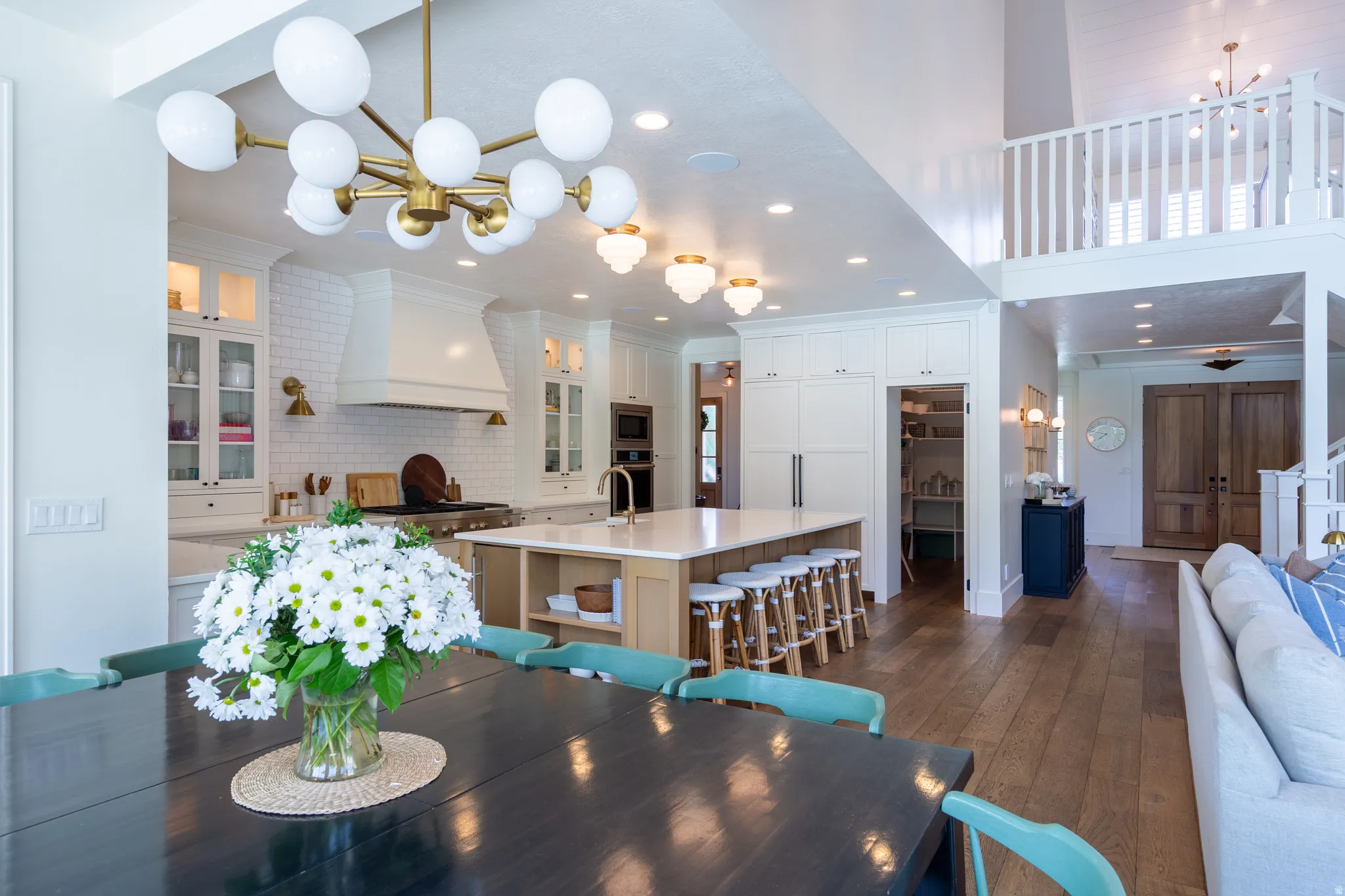 Open-concept kitchen and dining area featuring a custom range hood, white subway tile backsplash, a large center island with seating, and wood-finish flooring