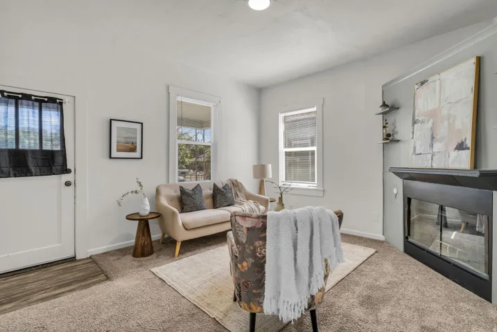 Living area featuring a fireplace with a black mantel, two windows with white trim, and light-colored carpeting