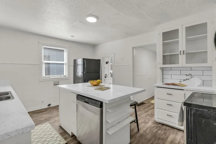 Bright kitchen featuring a central island with a built-in dishwasher, white countertops, a double basin stainless steel sink, and wood-finish flooring