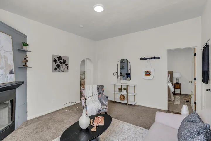Carpeted living area featuring a fireplace with built-in shelving, an arched doorway, and an open doorway to an additional room