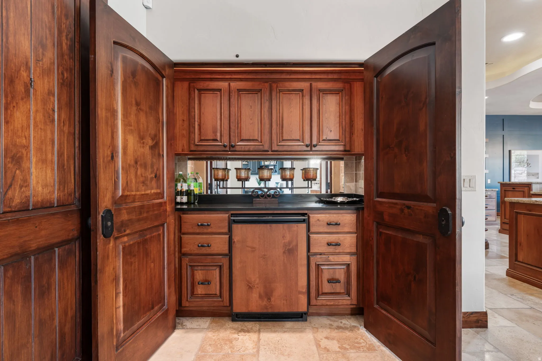Built-in wet bar featuring custom wood cabinetry, dark countertop, mirrored backsplash, under-cabinet lighting, and a compact integrated refrigerator