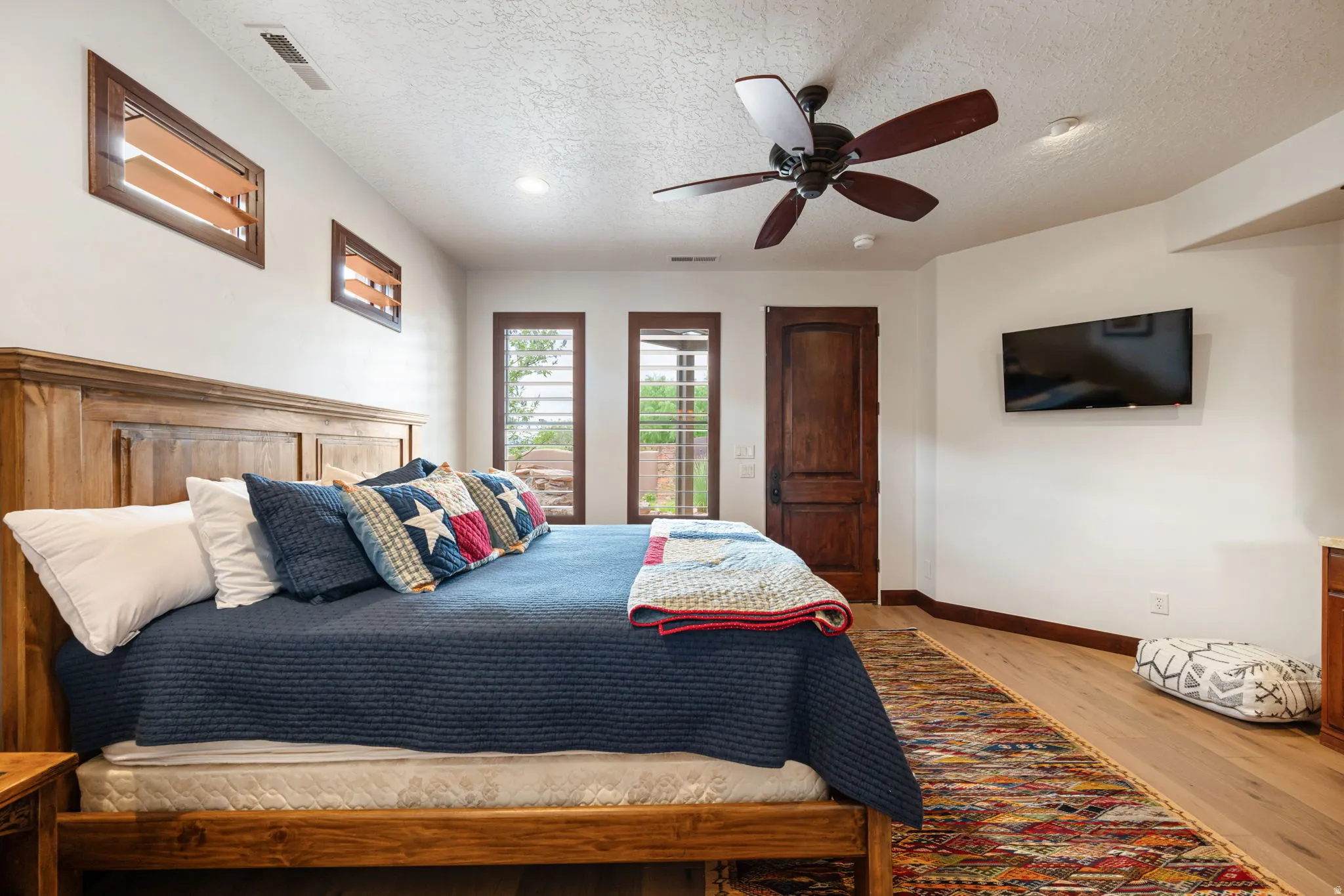 Spacious bedroom featuring wood-finish flooring, a built-in wood headboard, and multiple windows with wood frames
