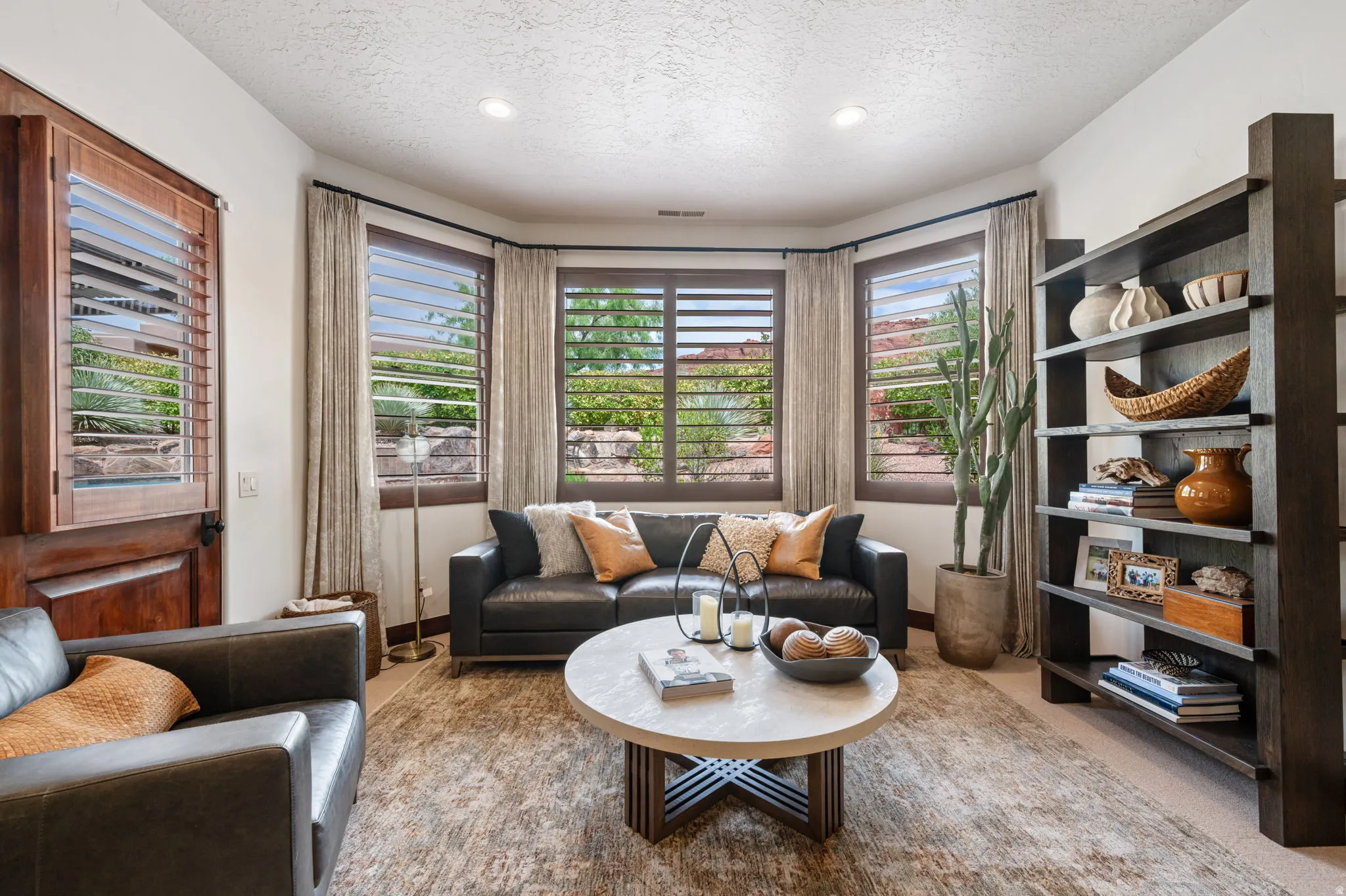 Living area featuring bay windows with wood plantation shutters and drapery, recessed lighting, and a built-in multi-shelf bookcase