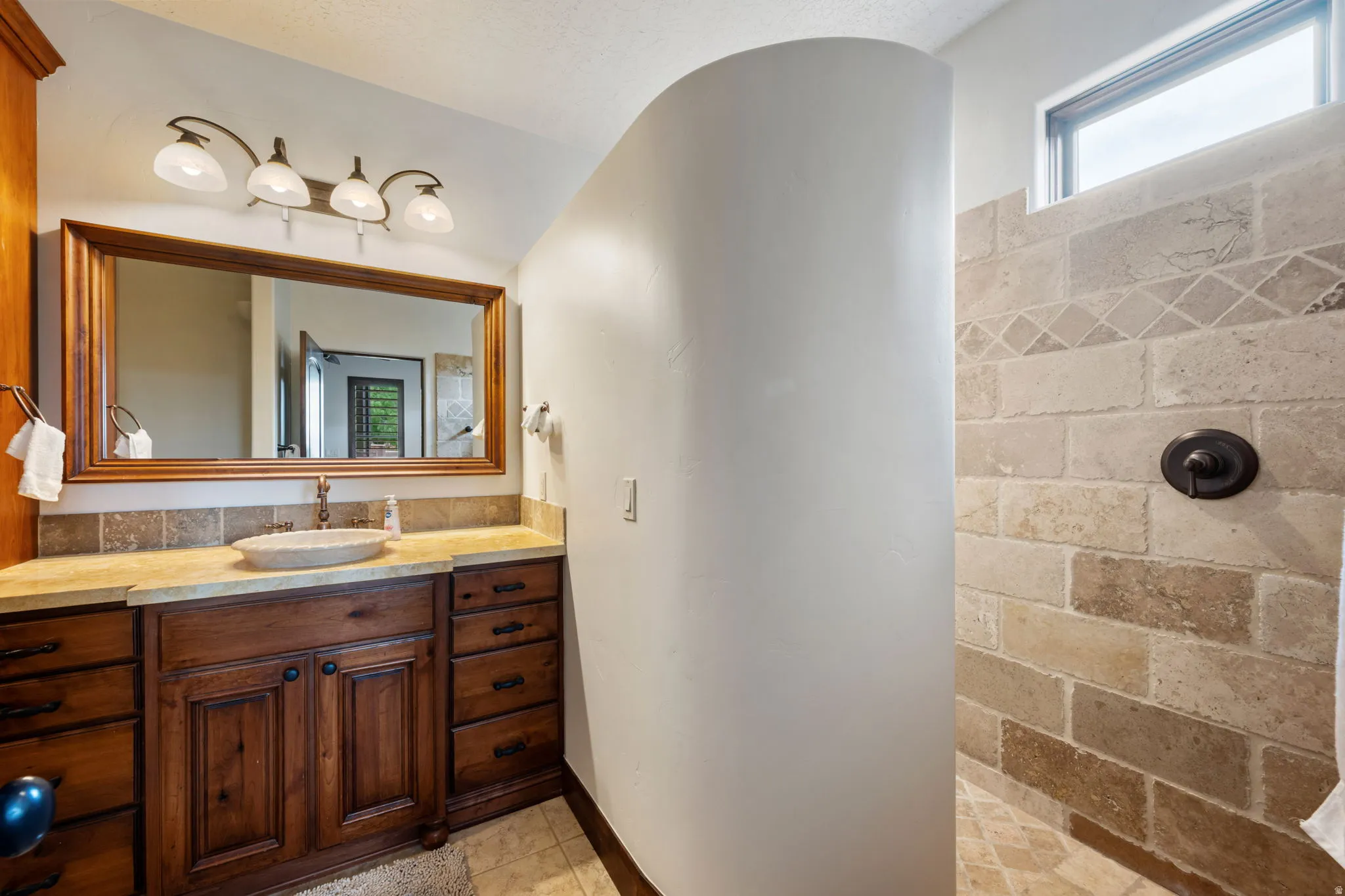 Bathroom featuring a stone vessel sink with a bronze faucet, a wood-framed mirror, and a four-light vanity fixture