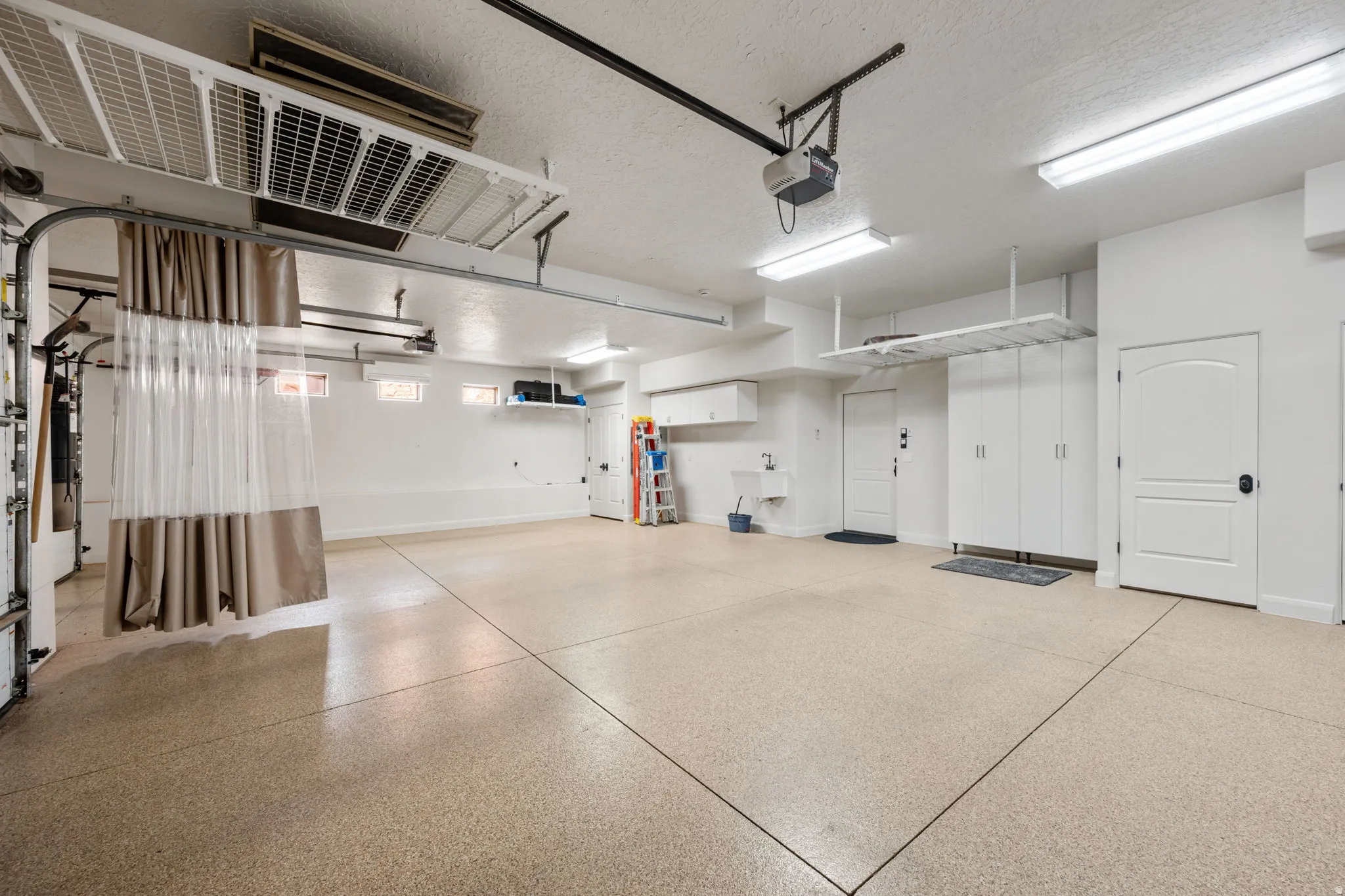 Spacious garage featuring epoxy flooring, built-in cabinetry, overhead storage racks, a utility sink, and multiple windows for natural light