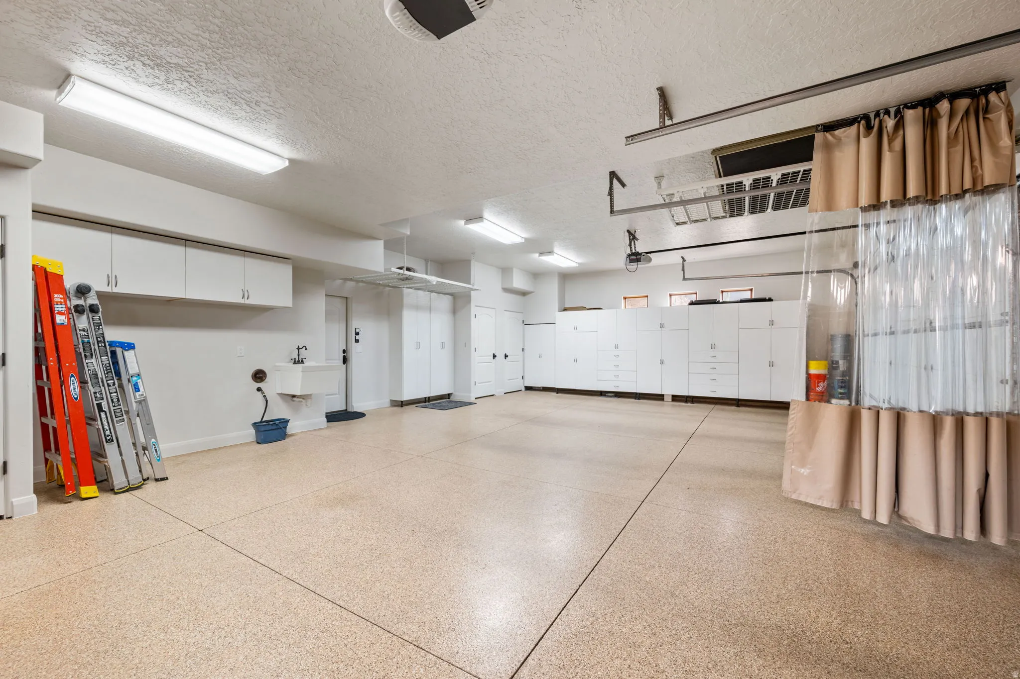 Spacious garage featuring a speckled epoxy floor coating, extensive built-in white cabinetry, a utility sink, and overhead fluorescent lighting