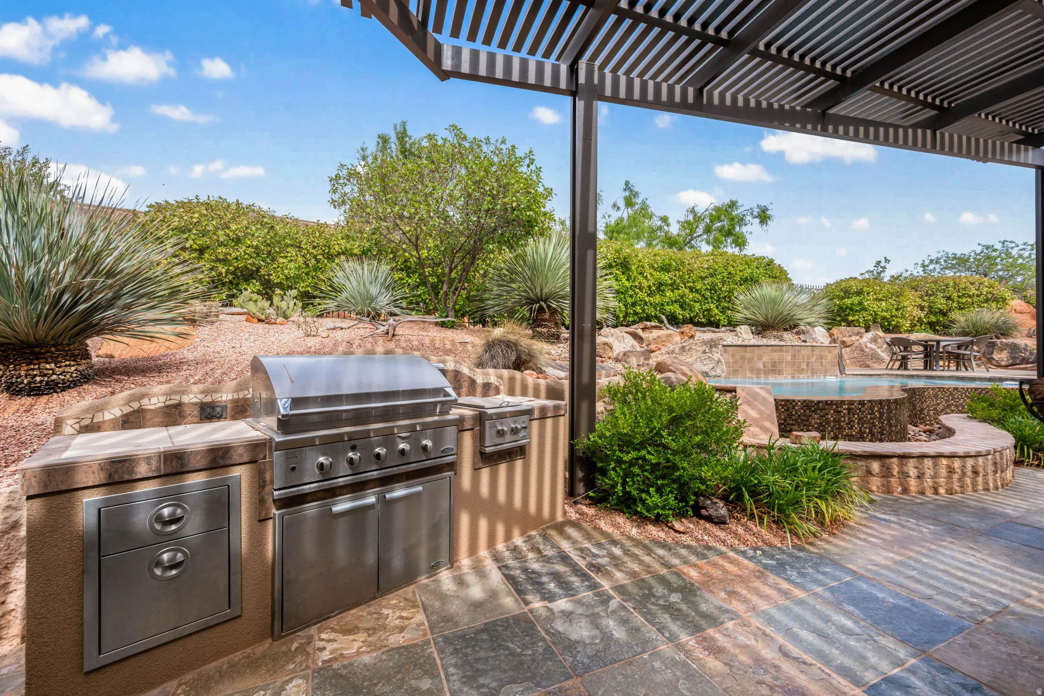 Outdoor kitchen featuring a built-in stainless steel grill and integrated storage, shaded by a louvered pergola