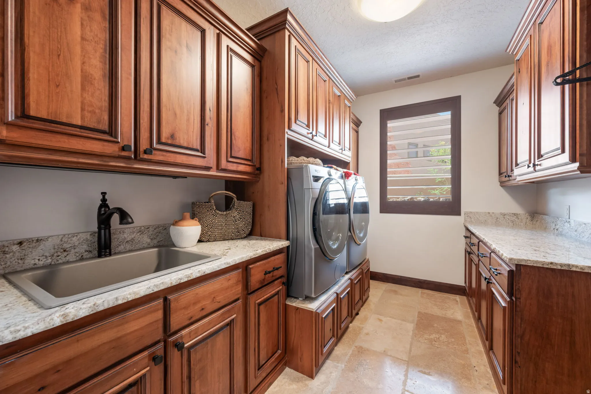 Laundry room featuring extensive wood cabinetry, light-toned stone tile flooring, and light-toned countertops