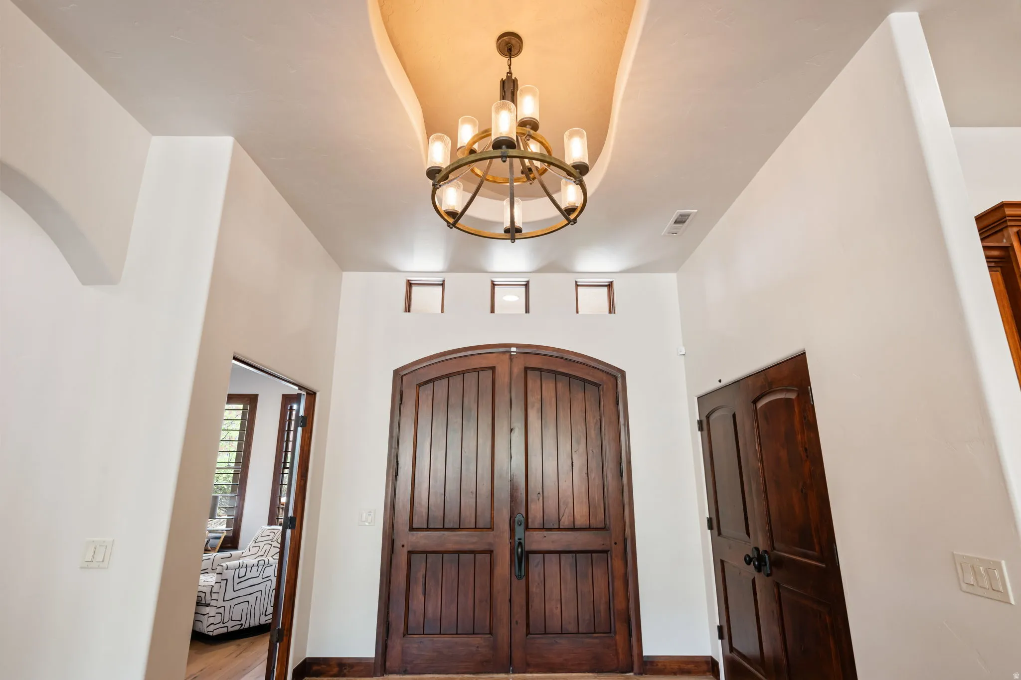 Grand entry featuring double arched wood doors with vertical paneling, an overhead chandelier, and a curved ceiling detail