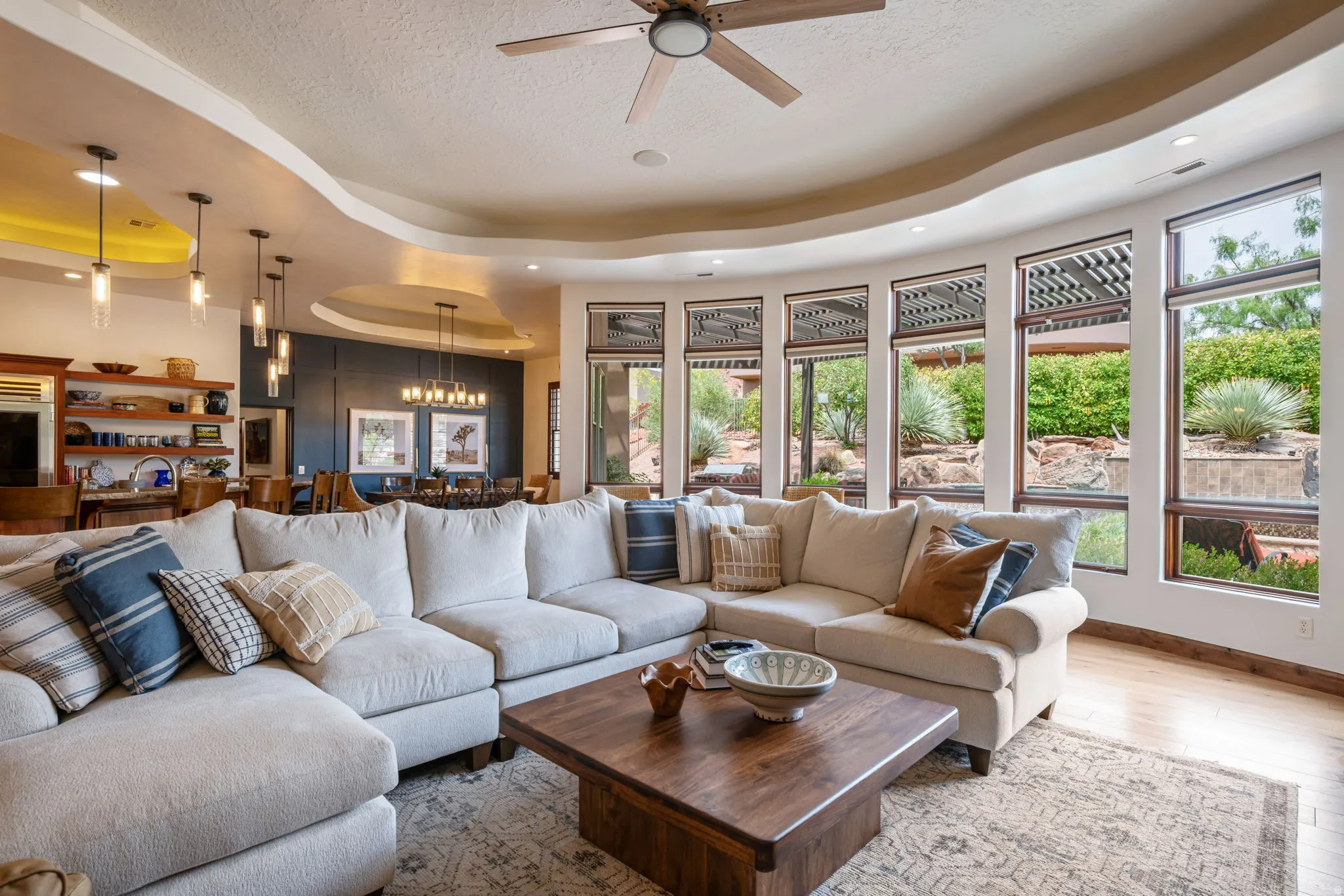 Living area with a curved wall of large windows, a tray ceiling with recessed lighting, and wood-finish flooring