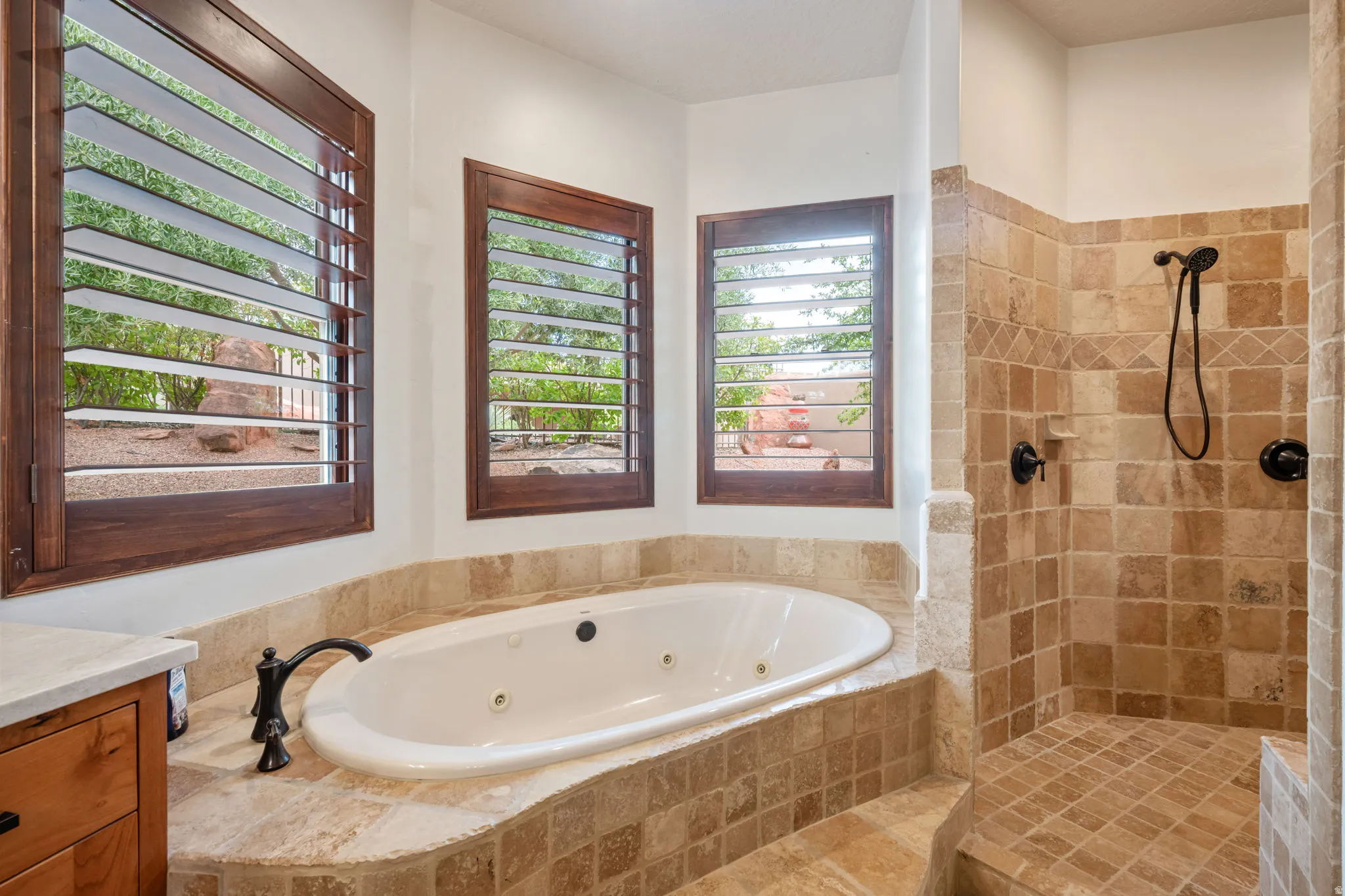 Jetted soaking tub with a deck-mounted faucet, surrounded by natural stone tile