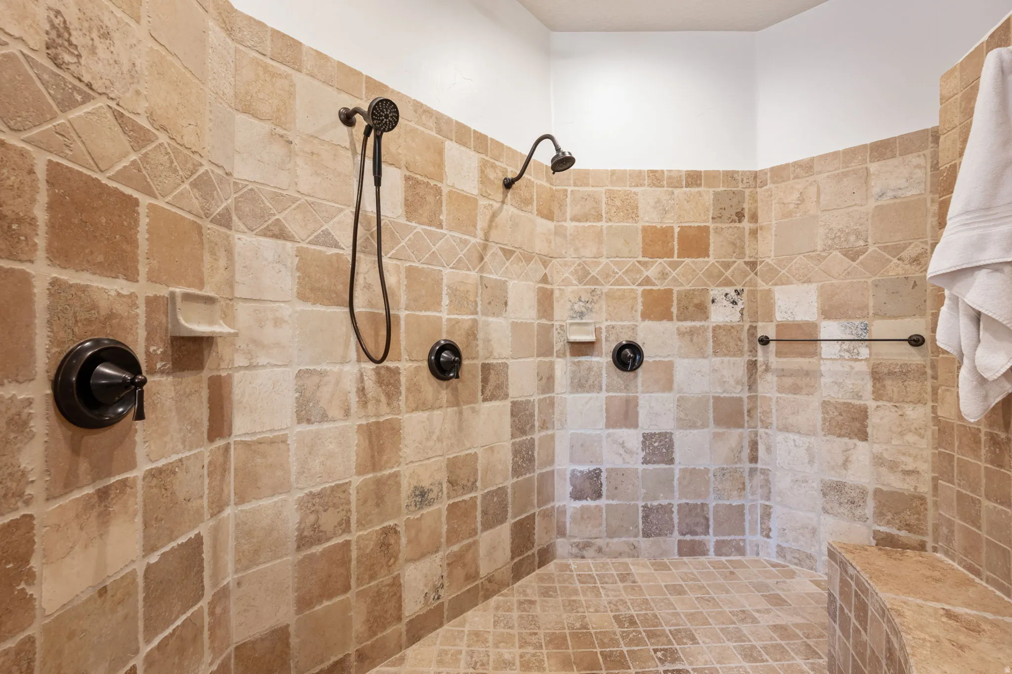 Expansive tiled shower featuring dual showerheads, one with a handheld sprayer, and rich bronze fixtures