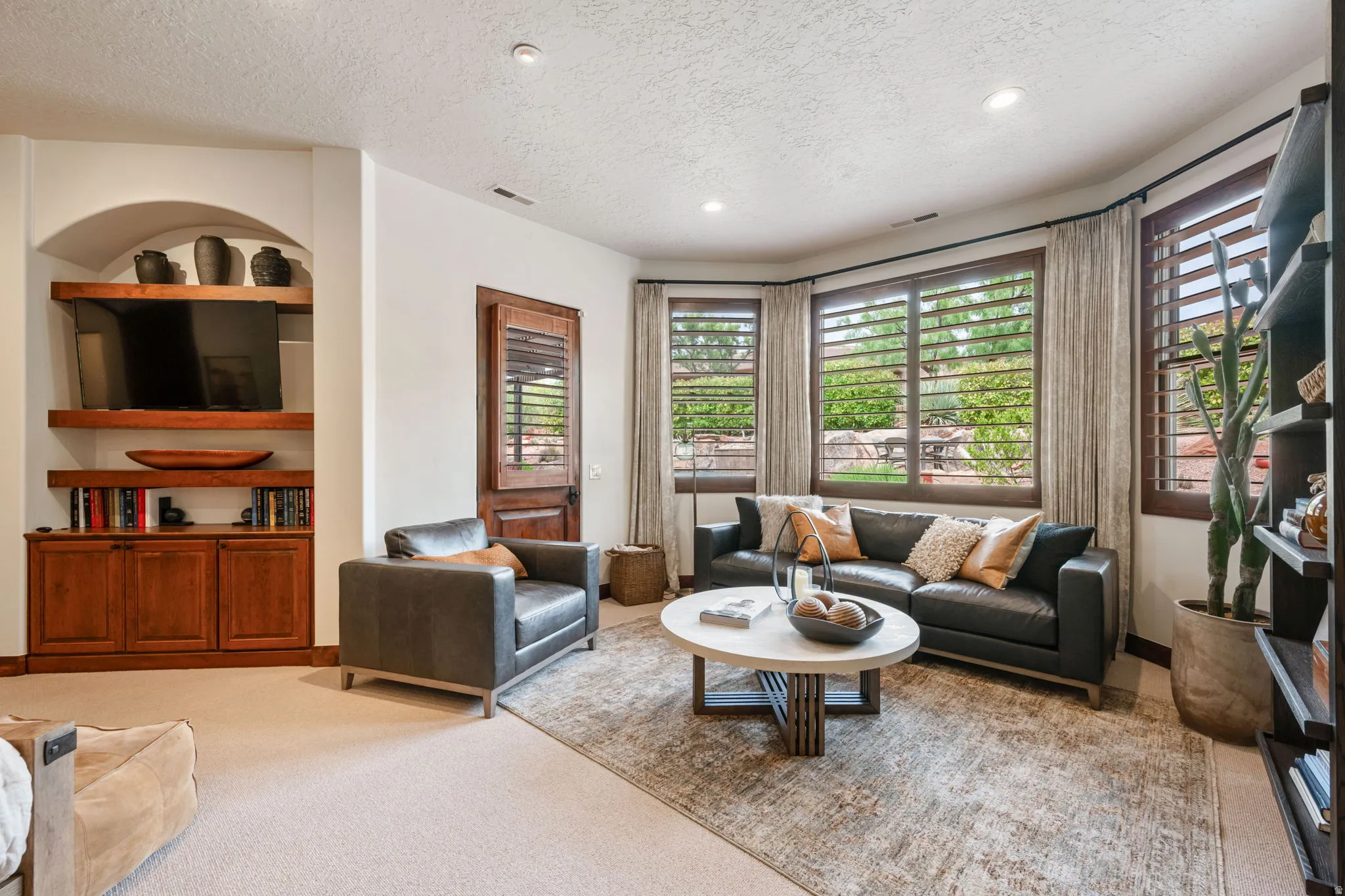 Living area featuring a custom built-in entertainment center with wood cabinetry and shelving, recessed lighting, and bay windows with plantation shutters