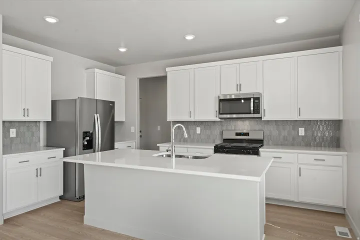 Modern kitchen featuring an expansive center island with an integrated sink, white cabinetry, stainless steel appliances, geometric tile backsplash, and recessed lighting