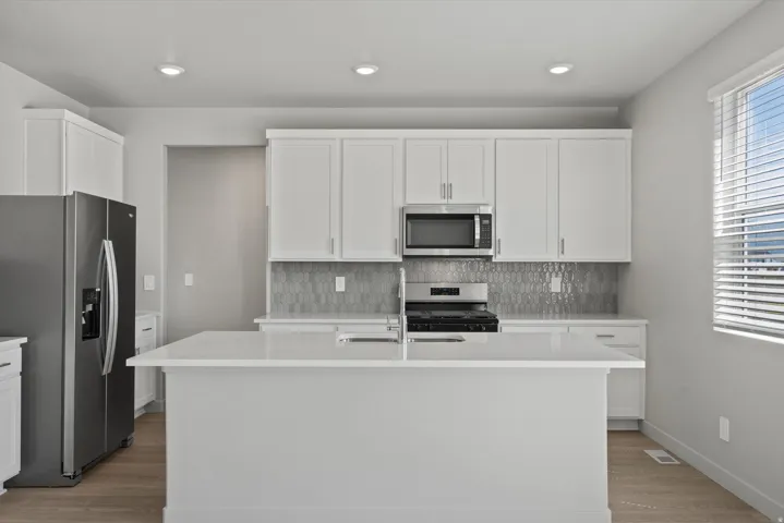 Contemporary kitchen featuring an expansive center island with an integrated sink, light-toned cabinetry, and stainless steel appliances
