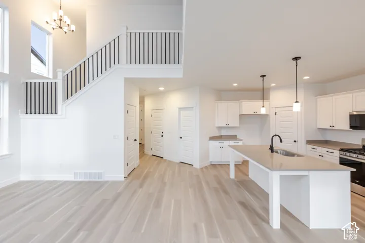 Open-concept living area with wood-finish flooring, a two-story ceiling, and a modern kitchen featuring white cabinetry and a central island