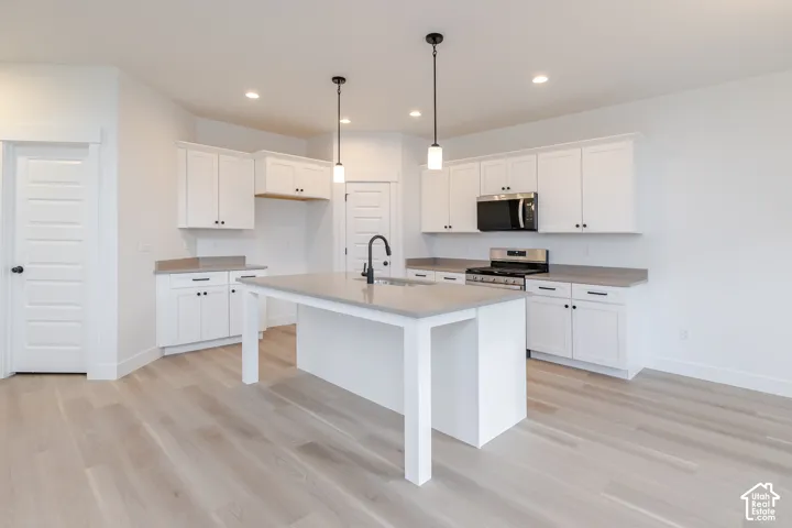 Open-concept kitchen featuring an island with counter seating, white cabinetry with black hardware, wood-finish flooring, recessed lighting, and pendant light fixtures