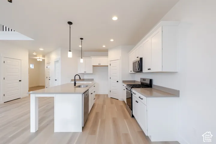 Modern kitchen featuring white cabinetry, light countertops, stainless steel appliances, and wood-finish flooring