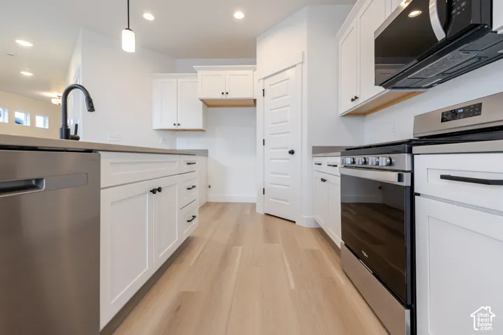 White shaker cabinetry, light wood-finish flooring, stainless steel appliances, dark countertops, and recessed lighting