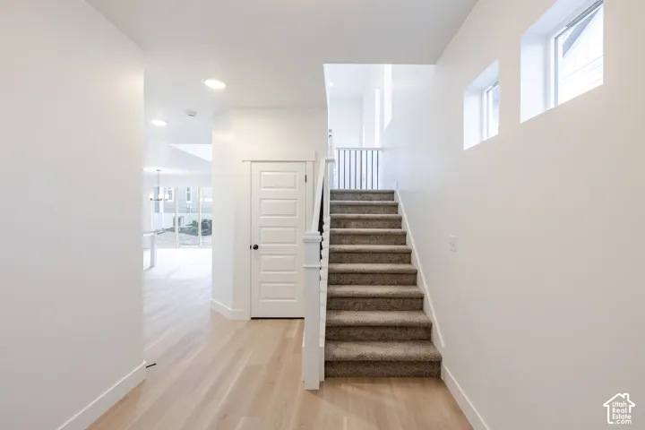 Bright entryway featuring wood-finish flooring, recessed lighting, and a carpeted staircase with white balusters