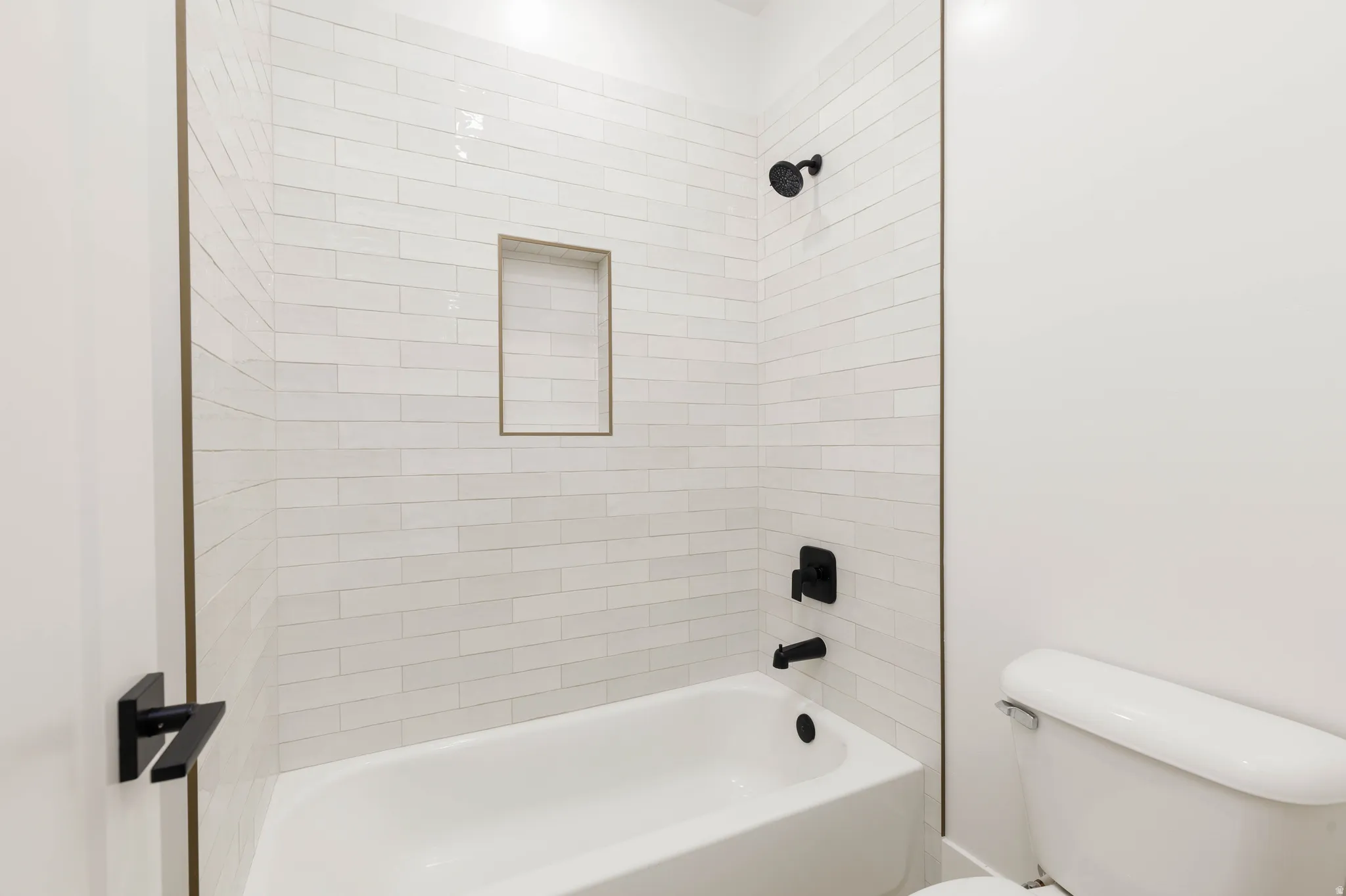 Bathtub shower with white subway tile surround, recessed niche, and matte black fixtures