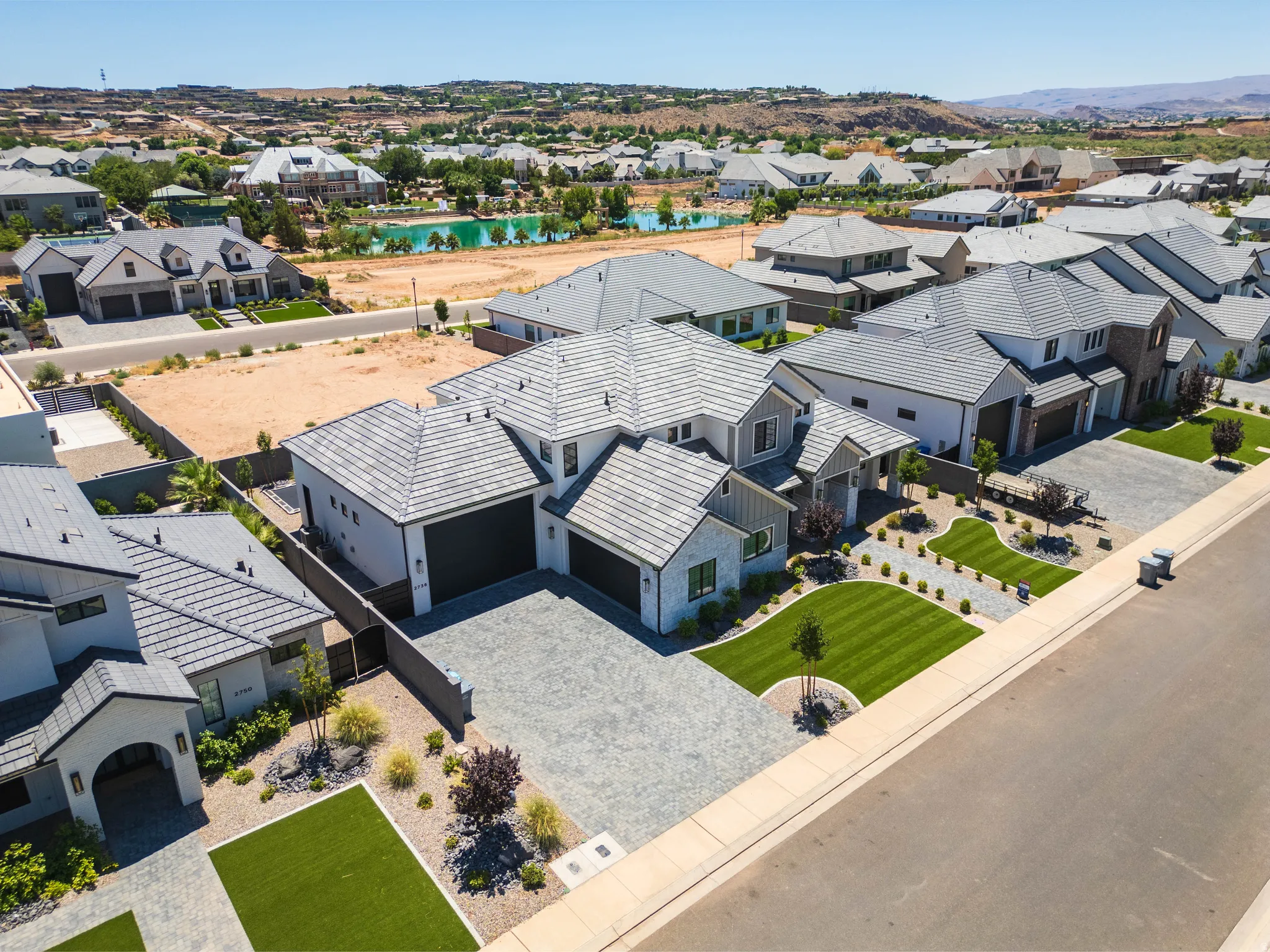 Modern-style residence featuring a patterned paver driveway, dark-tiled roof, and manicured landscaping with artificial turf accents