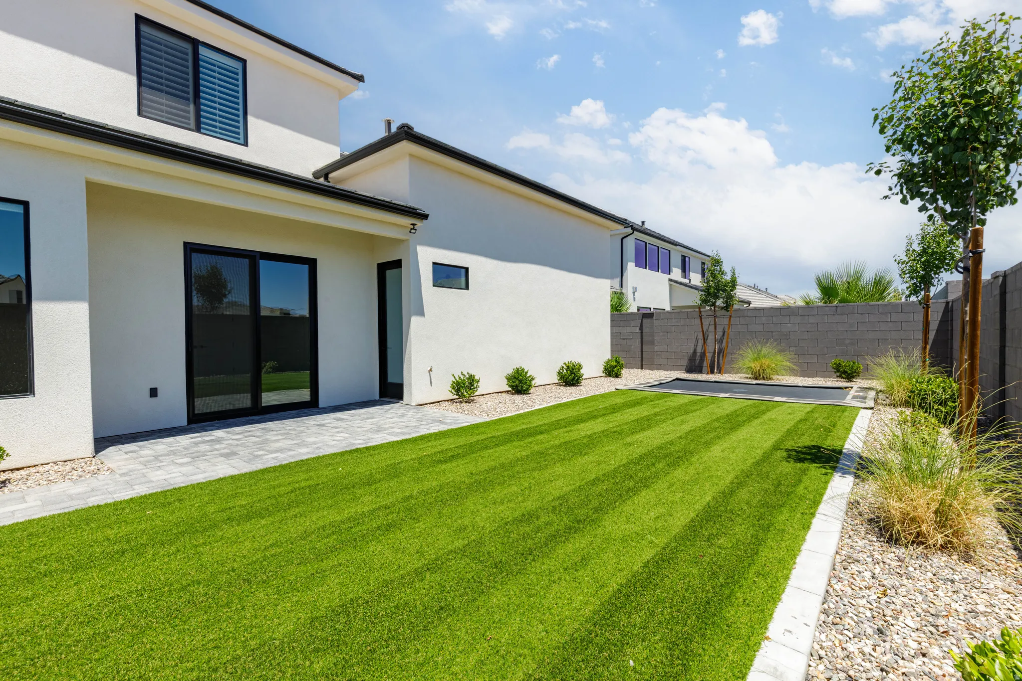 Expansive backyard featuring a striped artificial turf lawn, paver patio, and mature landscaping
