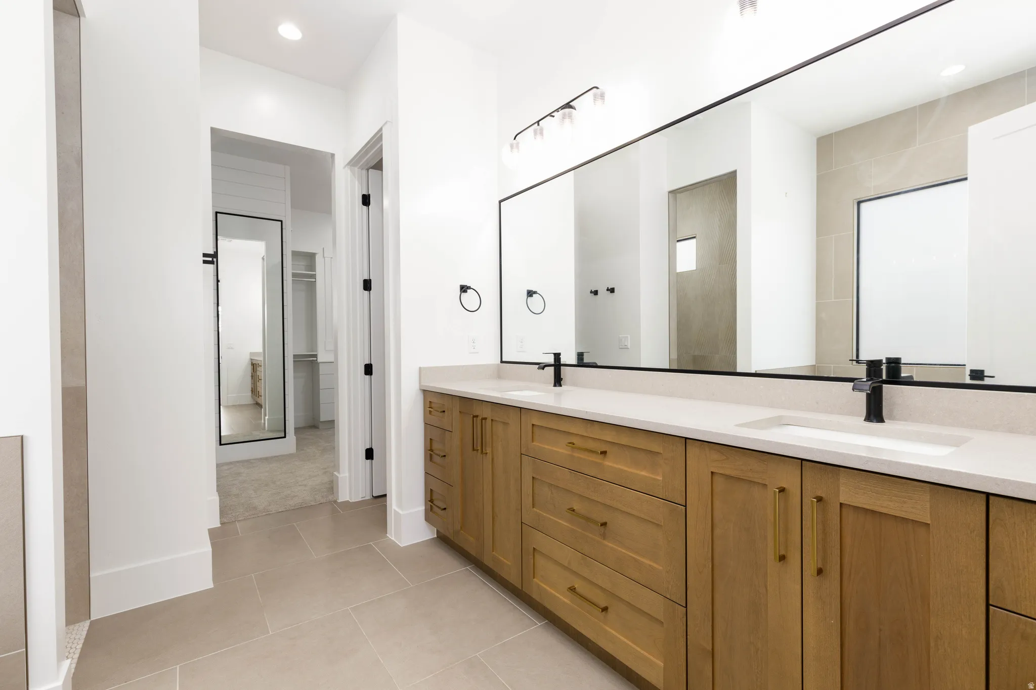 Dual vanity featuring light wood-finish cabinetry, gold-tone hardware, and white countertops