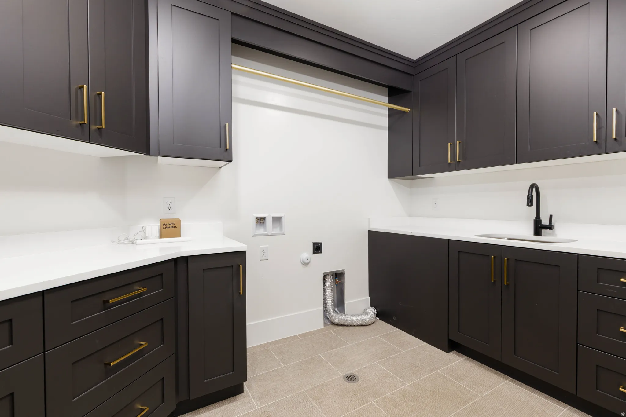 Laundry space featuring dark shaker-style cabinetry with brass hardware, white countertops, and a utility sink with a matte black faucet