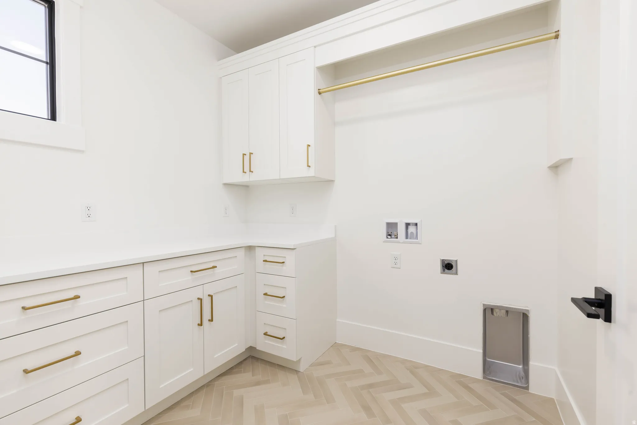 Utility room featuring white cabinetry with gold-finish hardware, light wood-finish herringbone flooring, a built-in hanging rod, and a window for natural light