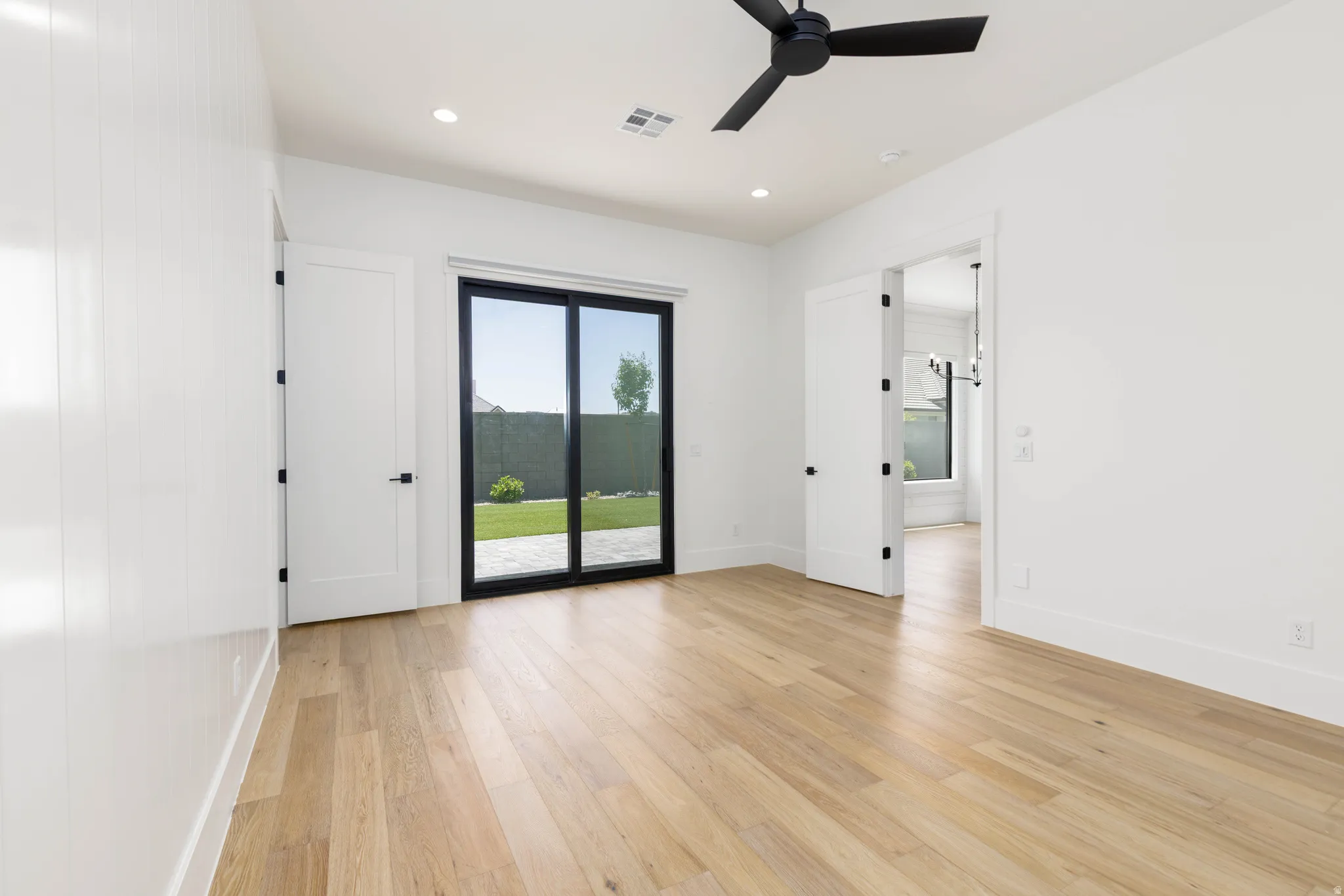 Spacious room featuring light wood-finish flooring, white walls, and a black ceiling fan