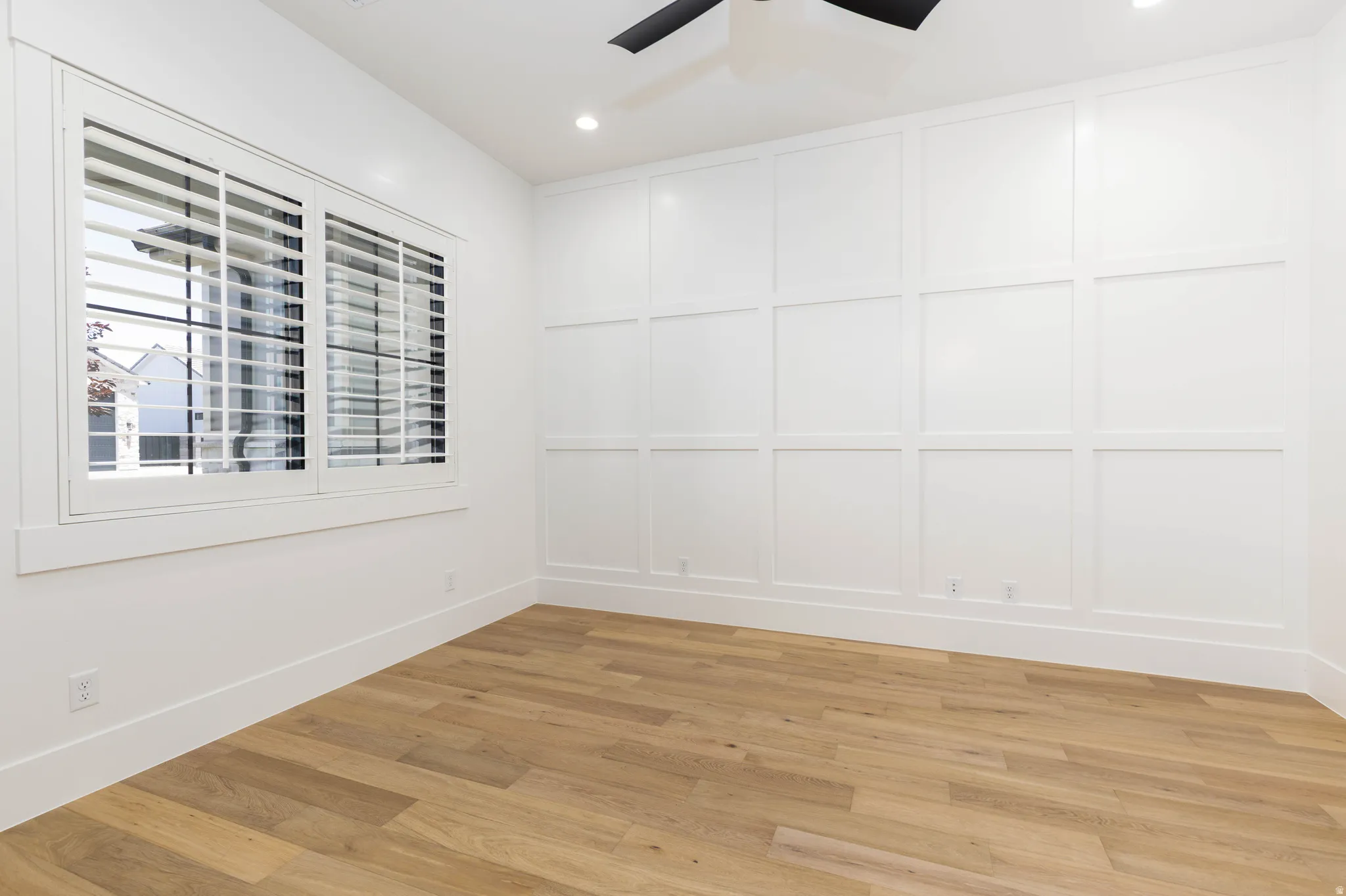 Room featuring a panel accent wall, wood-finish flooring, plantation shutters, recessed lighting, and a ceiling fan