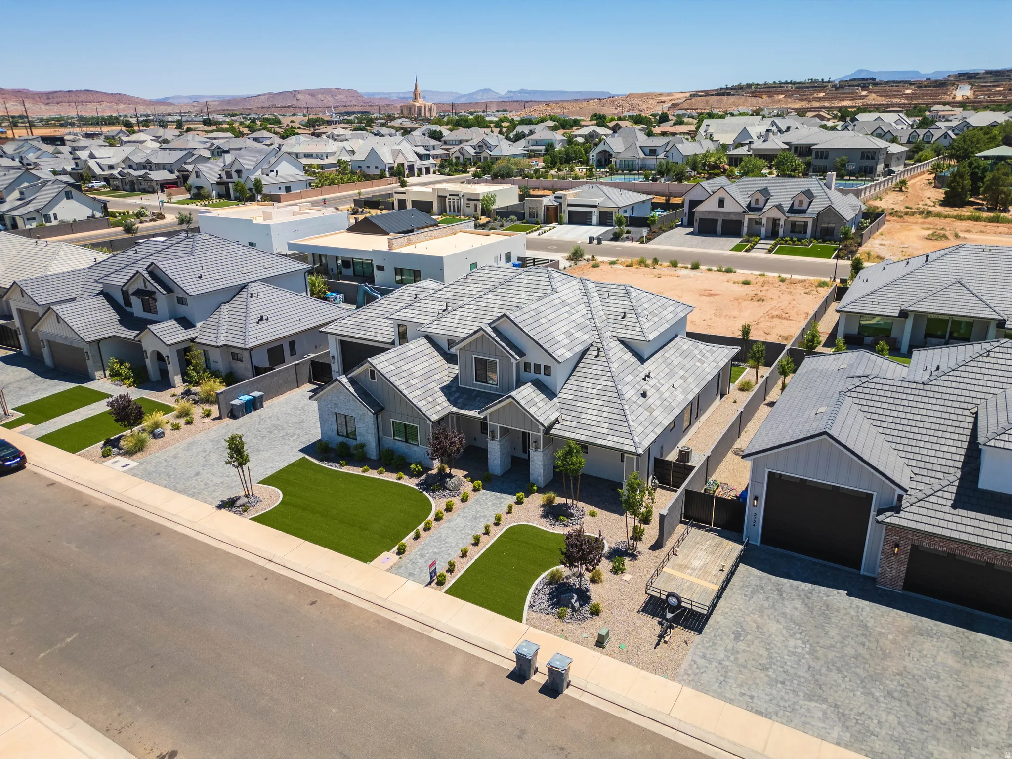 Contemporary architecture featuring an expansive paver driveway, artificial turf landscaping, and a multi-gabled roofline