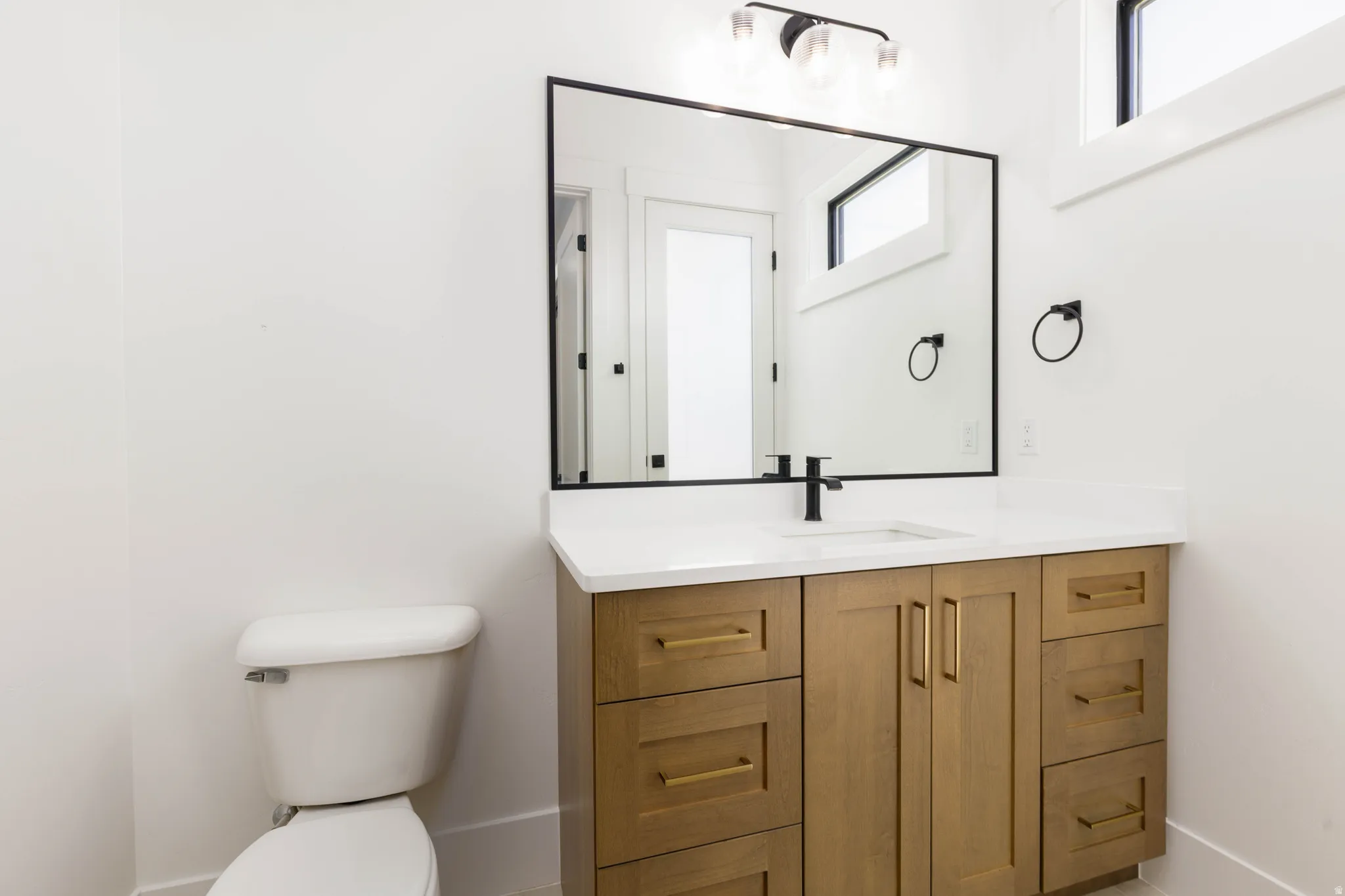 Bathroom vanity featuring wood-finish cabinetry with gold-tone hardware, a white countertop, and an undermount sink with a matte black faucet