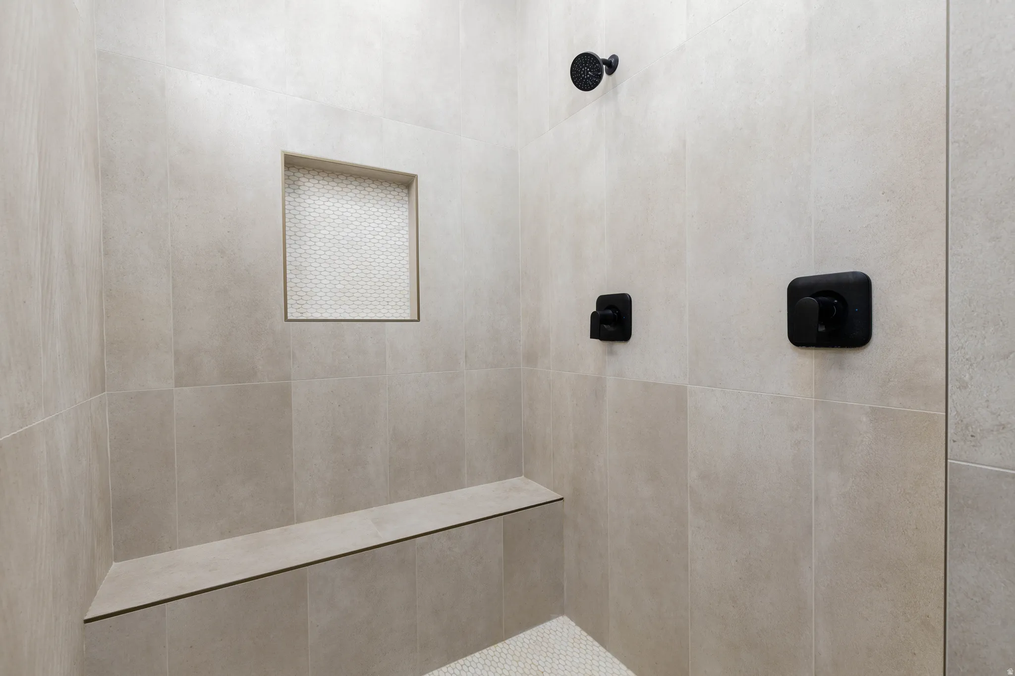 Shower stall featuring large format neutral-toned wall tiles, matte black fixtures, and a built-in bench