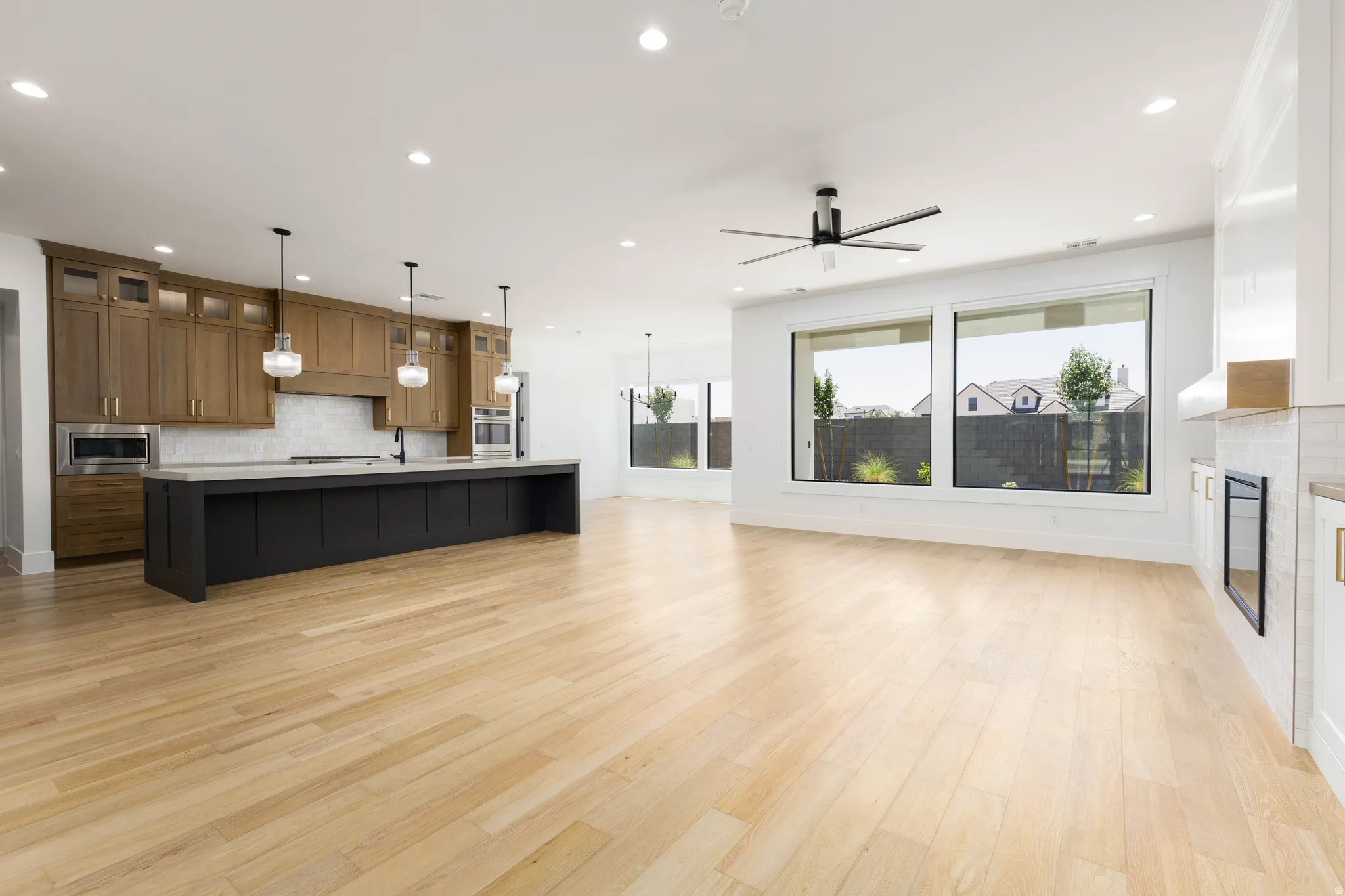 Open-concept living space featuring wood-finish flooring, a contemporary kitchen island with pendant lighting, recessed ceiling lights, and large windows
