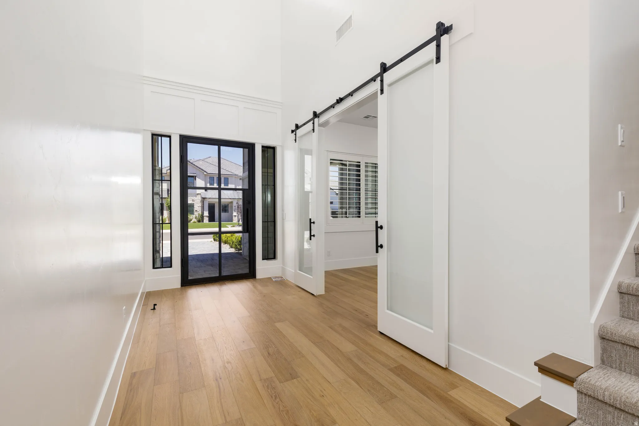 Entryway featuring a black-framed glass door with sidelights, wood-finish flooring, a white trim accent wall, and frosted glass barn doors