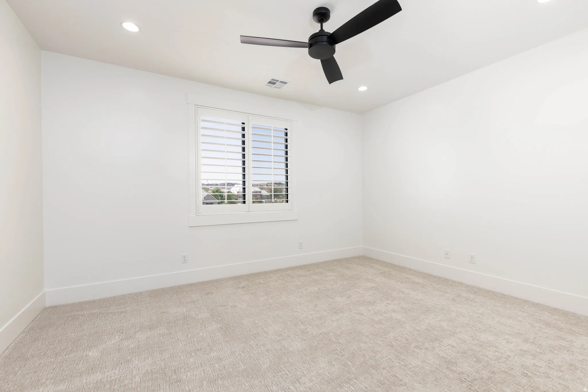 Bright interior space featuring a window with white louvered shutters, recessed lighting, a ceiling fan with black blades, and light-toned carpet flooring