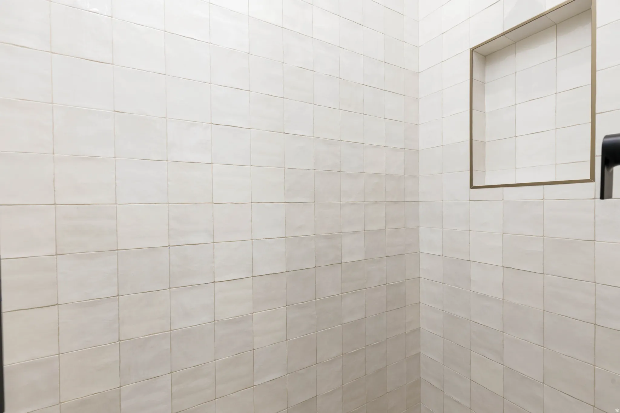 Tiled shower enclosure featuring light-toned square tiles and a recessed niche with a contrasting trim