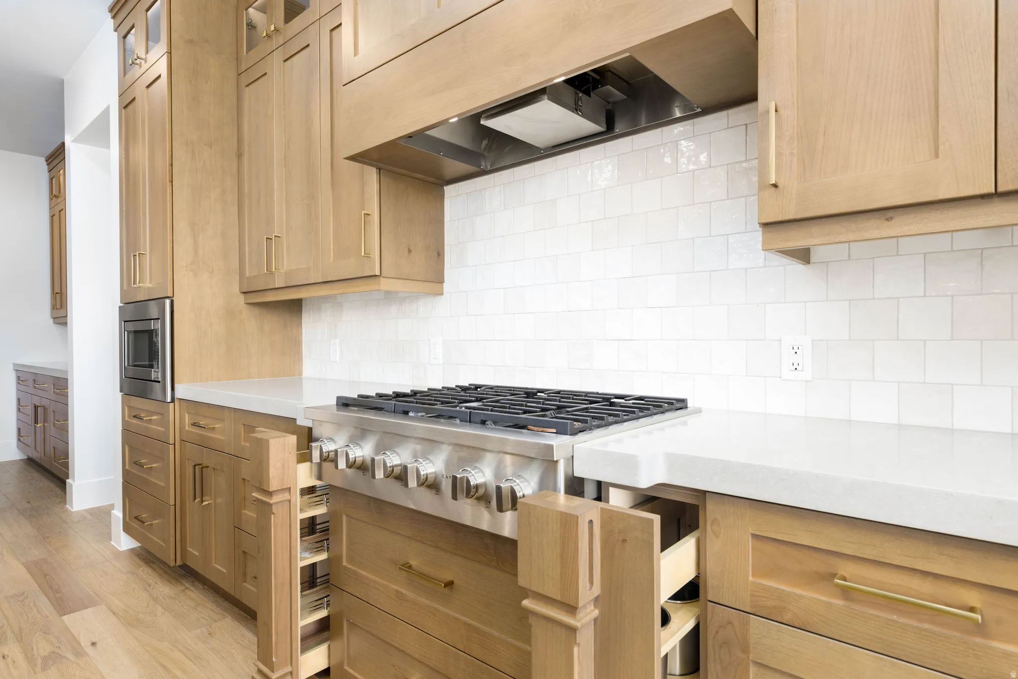 Gourmet kitchen features a professional-grade gas range, light wood-finish cabinetry, built-in microwave, white subway tile backsplash, and light-toned countertops
