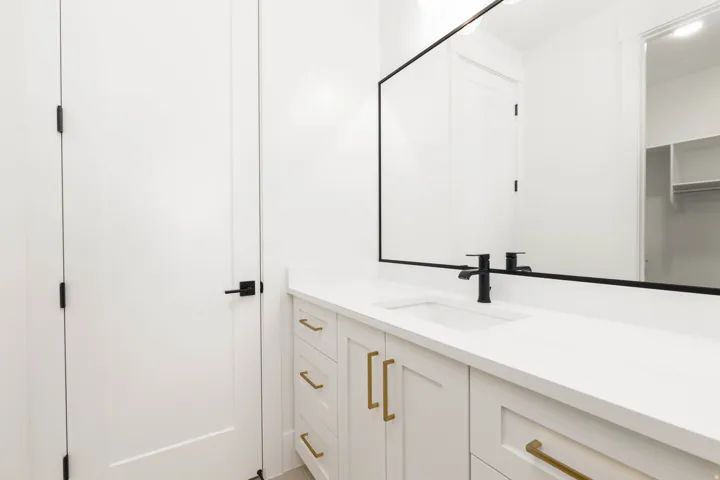 White vanity with gold-tone hardware, a white countertop, and an integrated rectangular sink