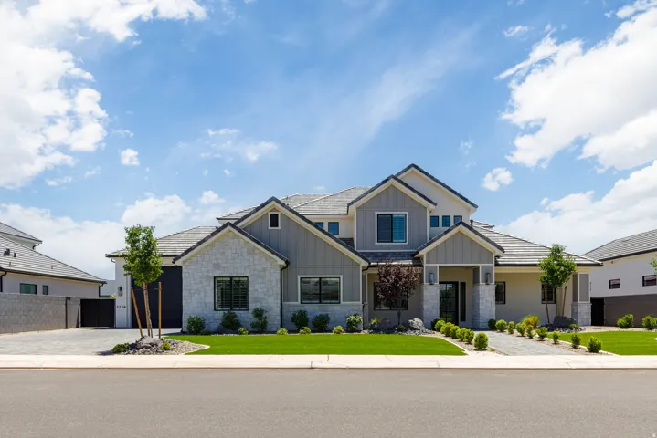 Contemporary two-story residence featuring a stone and board-and-batten facade, a tile roof, an integrated two-car garage, manicured front landscaping, and a paved driveway