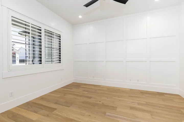 Room featuring a panel accent wall, wood-finish flooring, plantation shutters, recessed lighting, and a ceiling fan