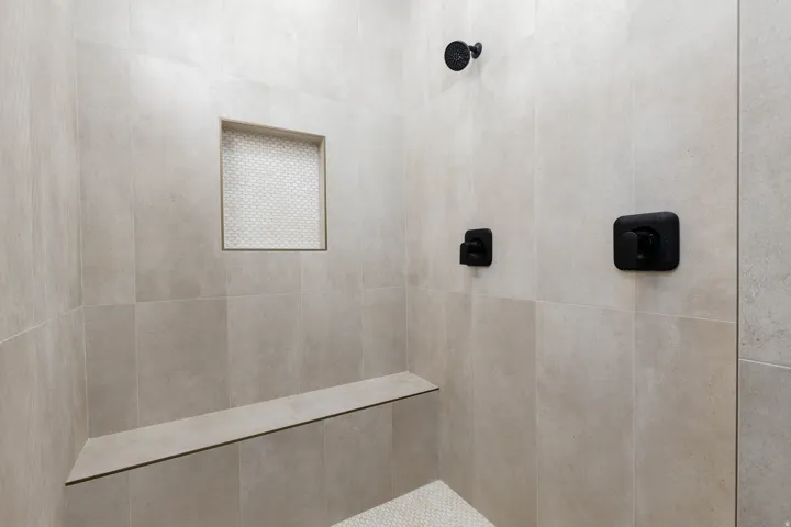 Shower stall featuring large format neutral-toned wall tiles, matte black fixtures, and a built-in bench