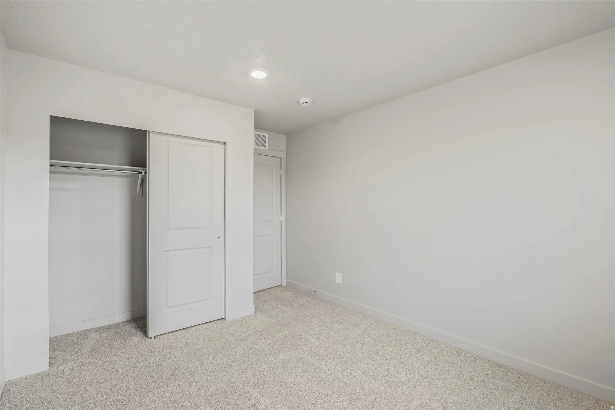 Neutral-toned room featuring light carpet flooring, white baseboards, and a built-in closet with sliding panel doors and a clothing rod