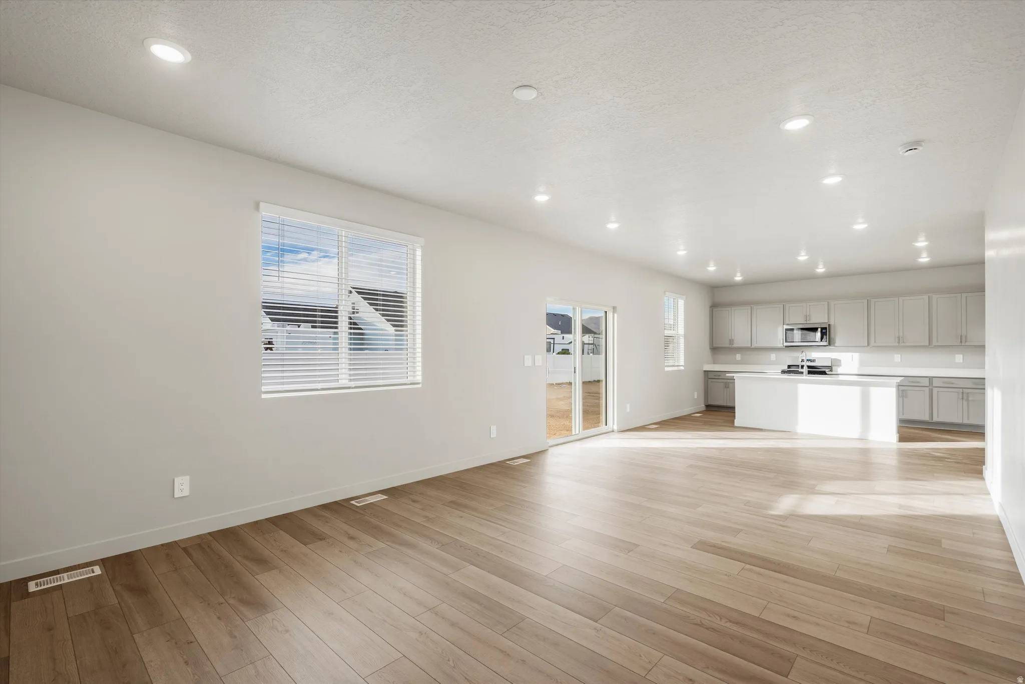 Spacious open-concept living area featuring wood-finish flooring, recessed lighting, and large windows with blinds